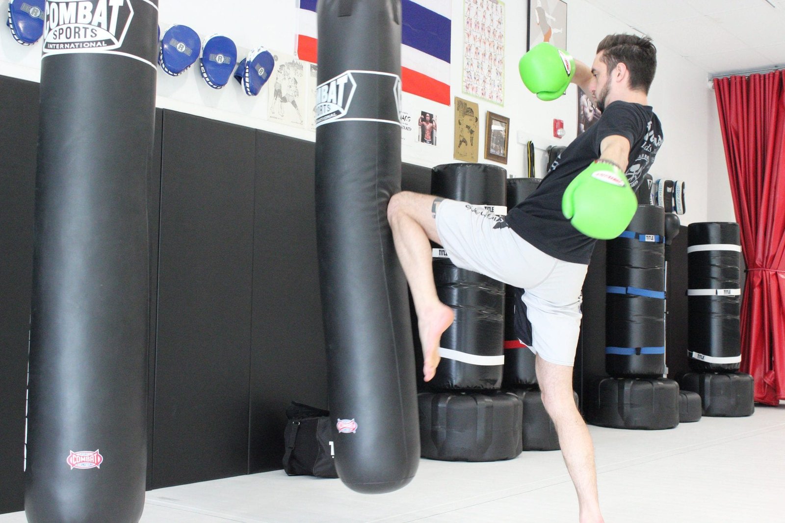 man in green gloves in light room kicking a heavy bag